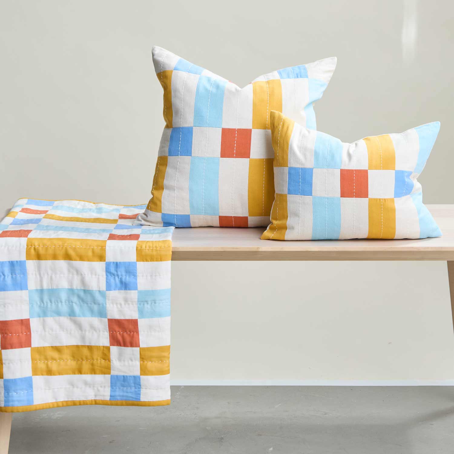 colorful checkered small pillows on light wooden bench with matching small quilt