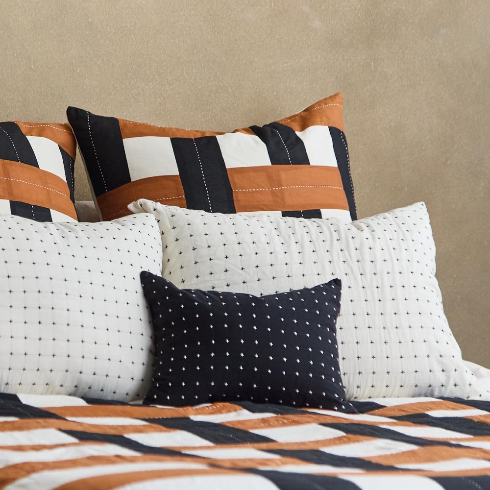 white cross-stitch pillow shams on bed with coordinating plaid black and camel euro shams