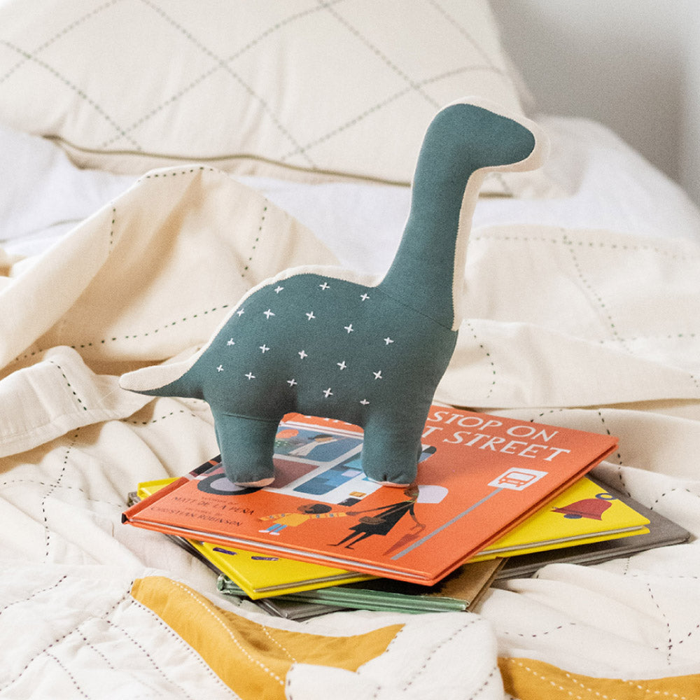 spruce green stuffed dinosaur on all white bed with embroidery