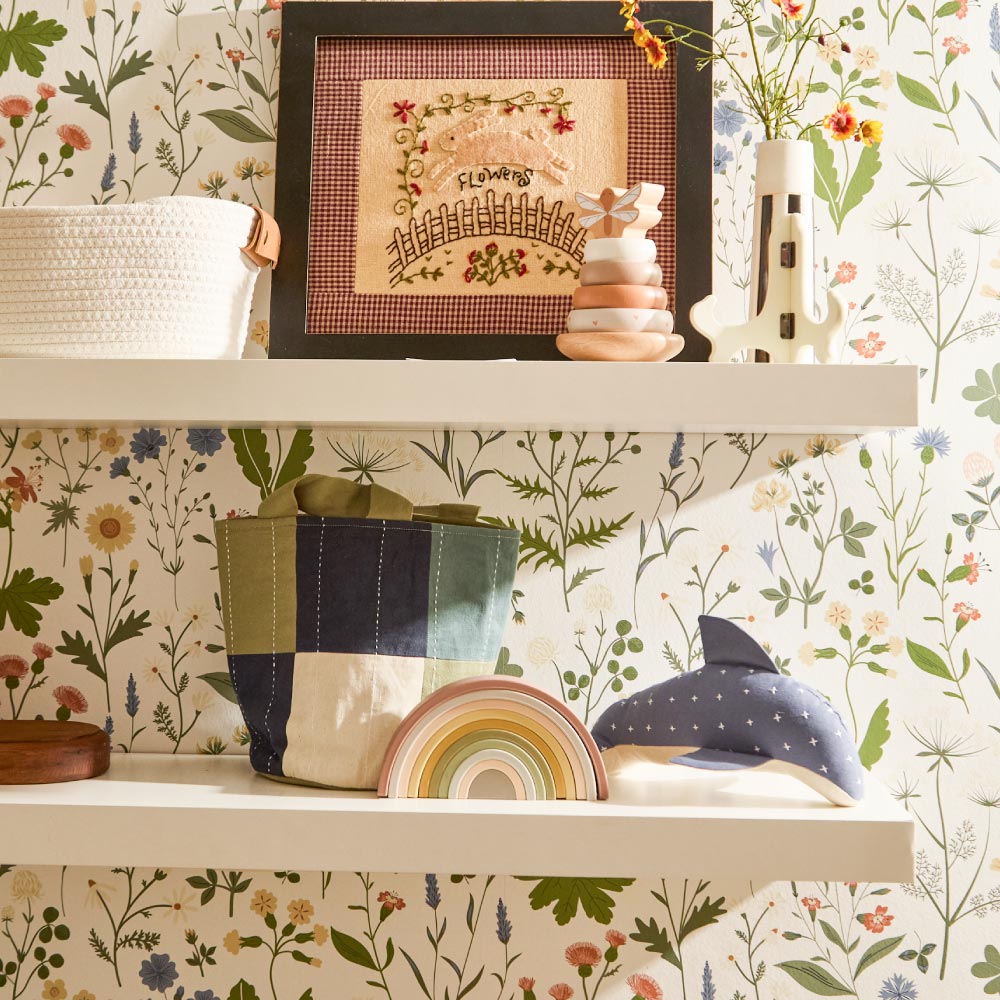 fabric storage bin and dolphin stuffed animal sitting on white wooden shelves in nursery with floral wallpaper