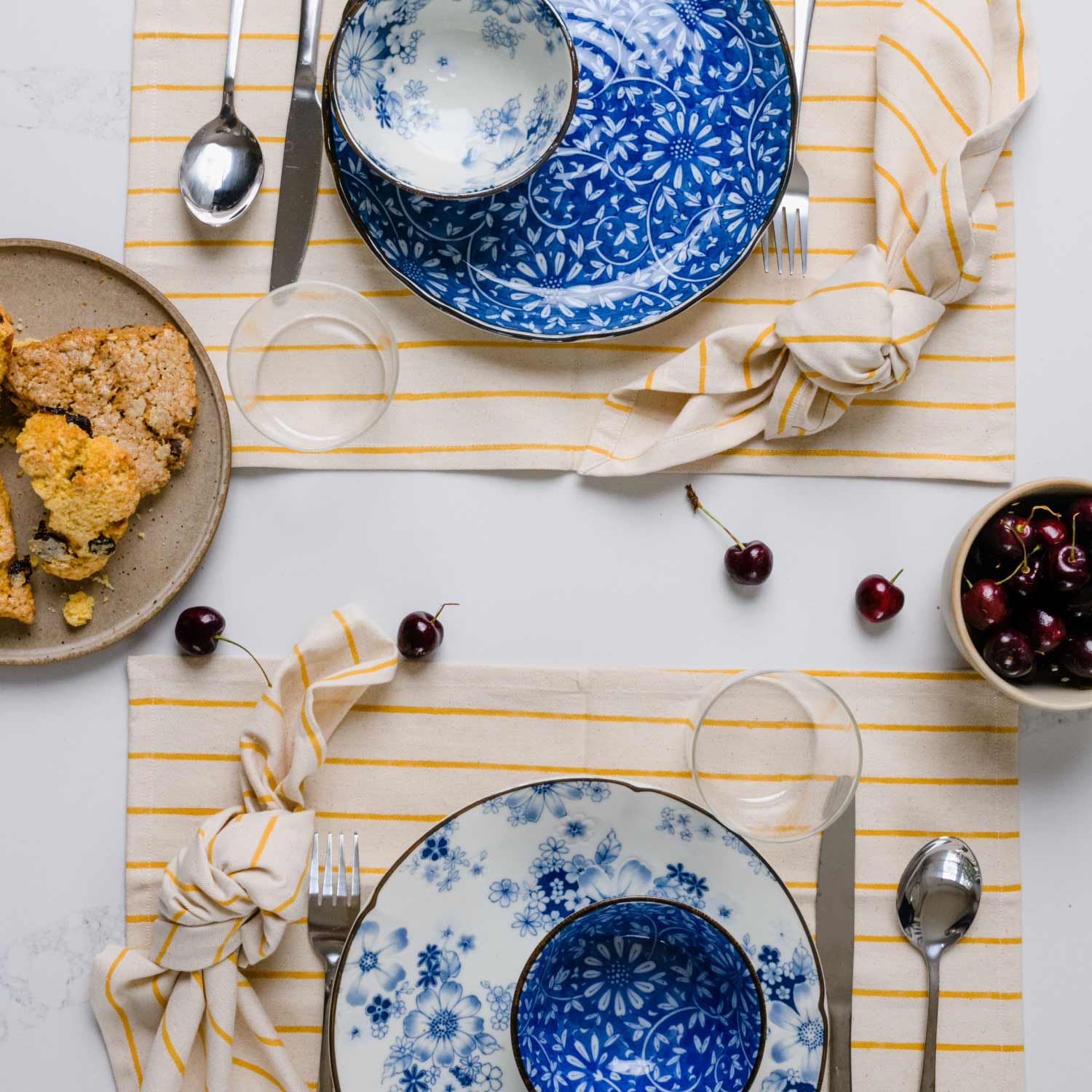 table setting for two with blue plates and mustard yellow striped placemats