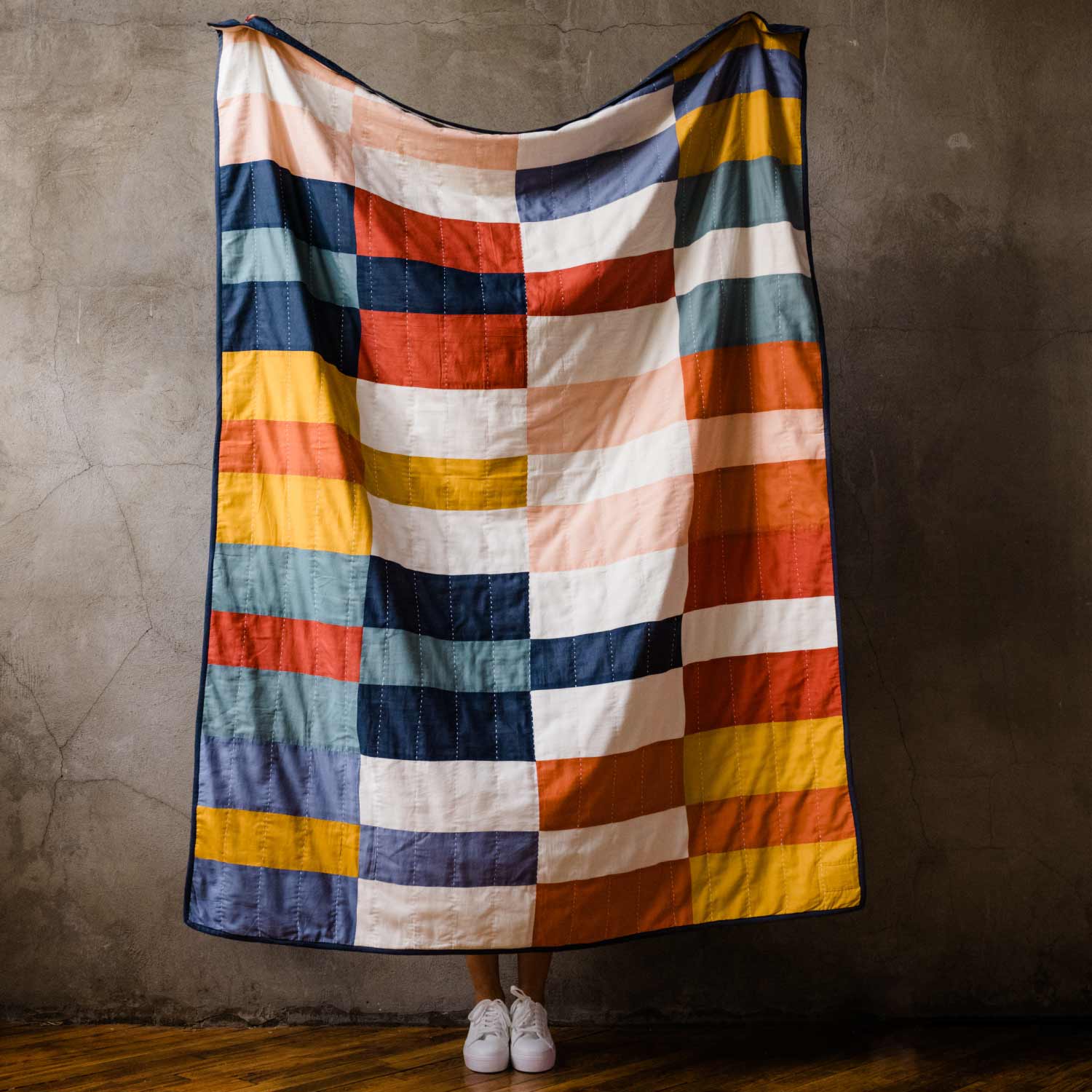 checkered patchwork quilt being held up against a cement wall