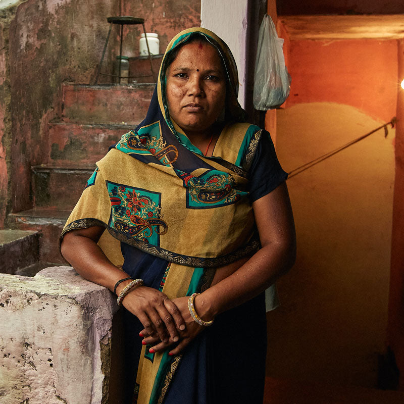 portrait of Senior artisan Manju standing in front of the doorway of her home in Ajmer, India