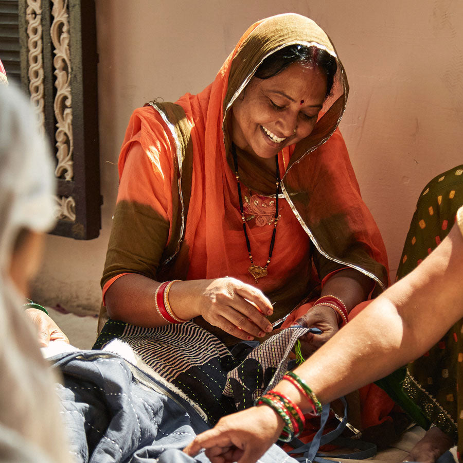 Senior artisan Neetu wearing orange sari hand-embroidering a kantha quilt in Ajmer, India