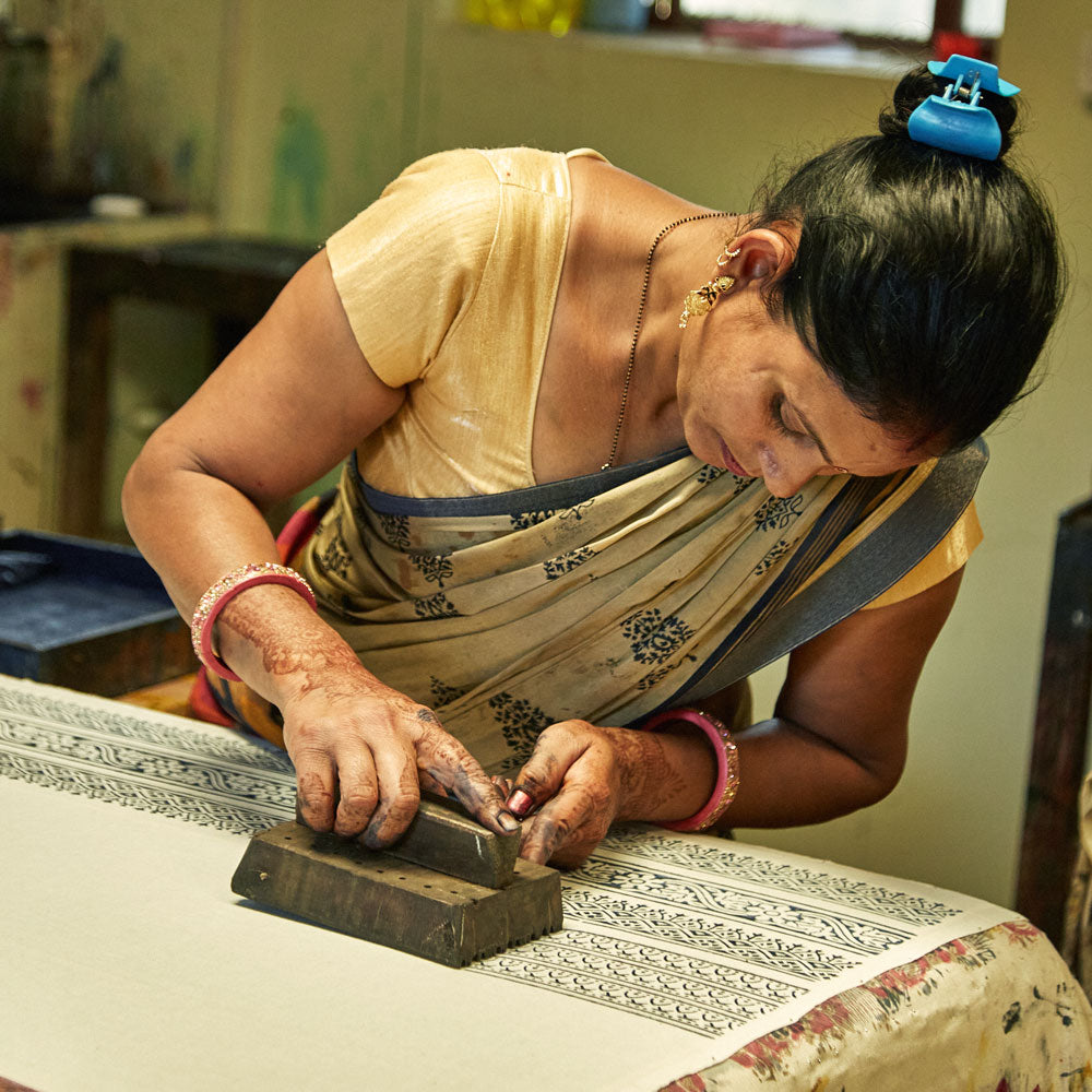 artisan using a carved wooden block to block print intricate pattern onto white organic cotton fabric