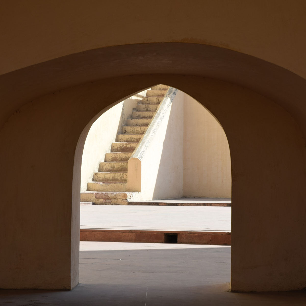 a curved shadowed archway with brightly lit stairs peaking through the doorway