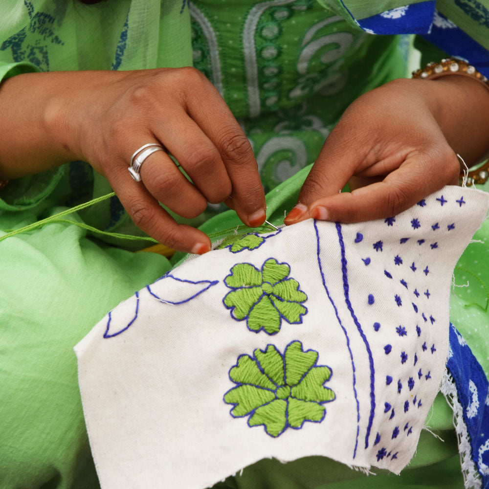 close up of hands embroidering textile art with embroidered lime green and royal blue flowers