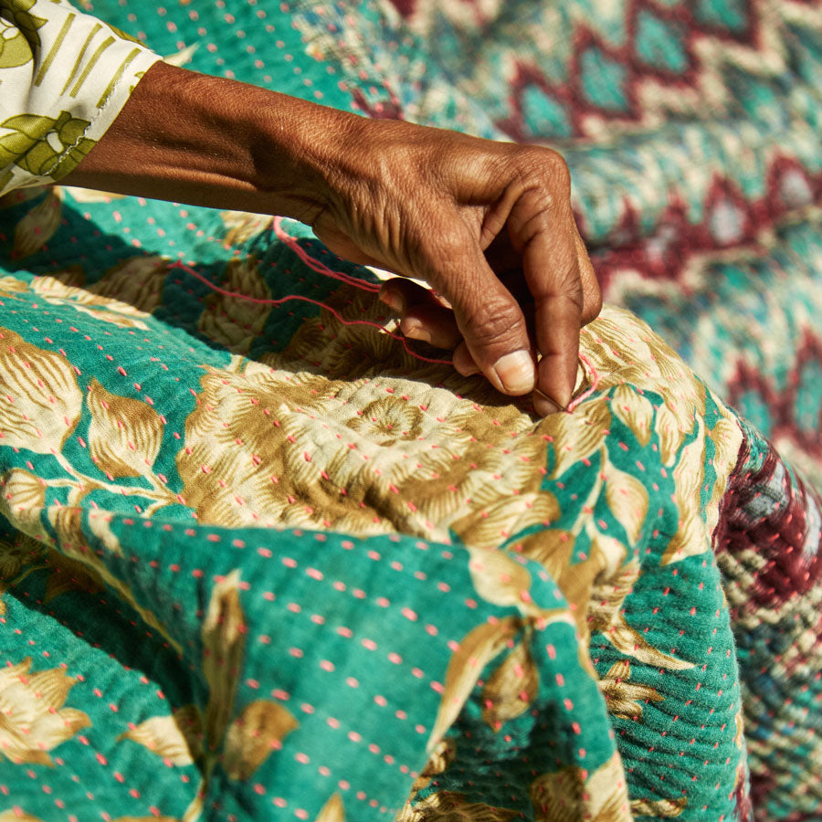 close up of hand of Anchal artisan with a needle and pink thread hand-stitching a kantha quilt