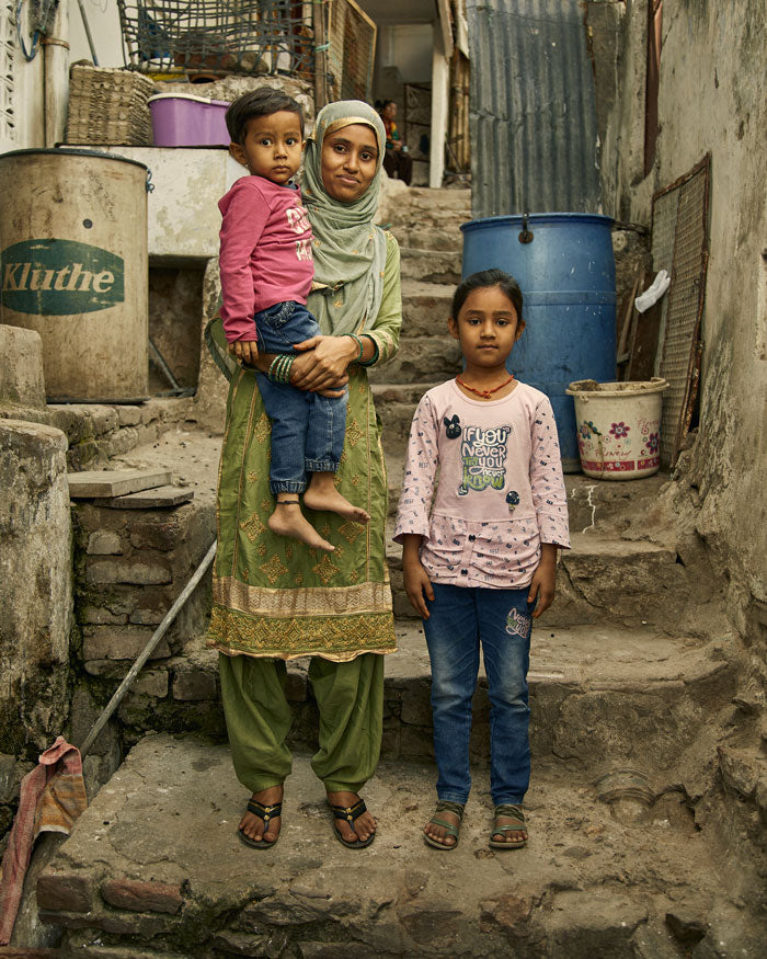 woman artisan in Ajmer, India standing with her two small children on stone stairs outside of her home