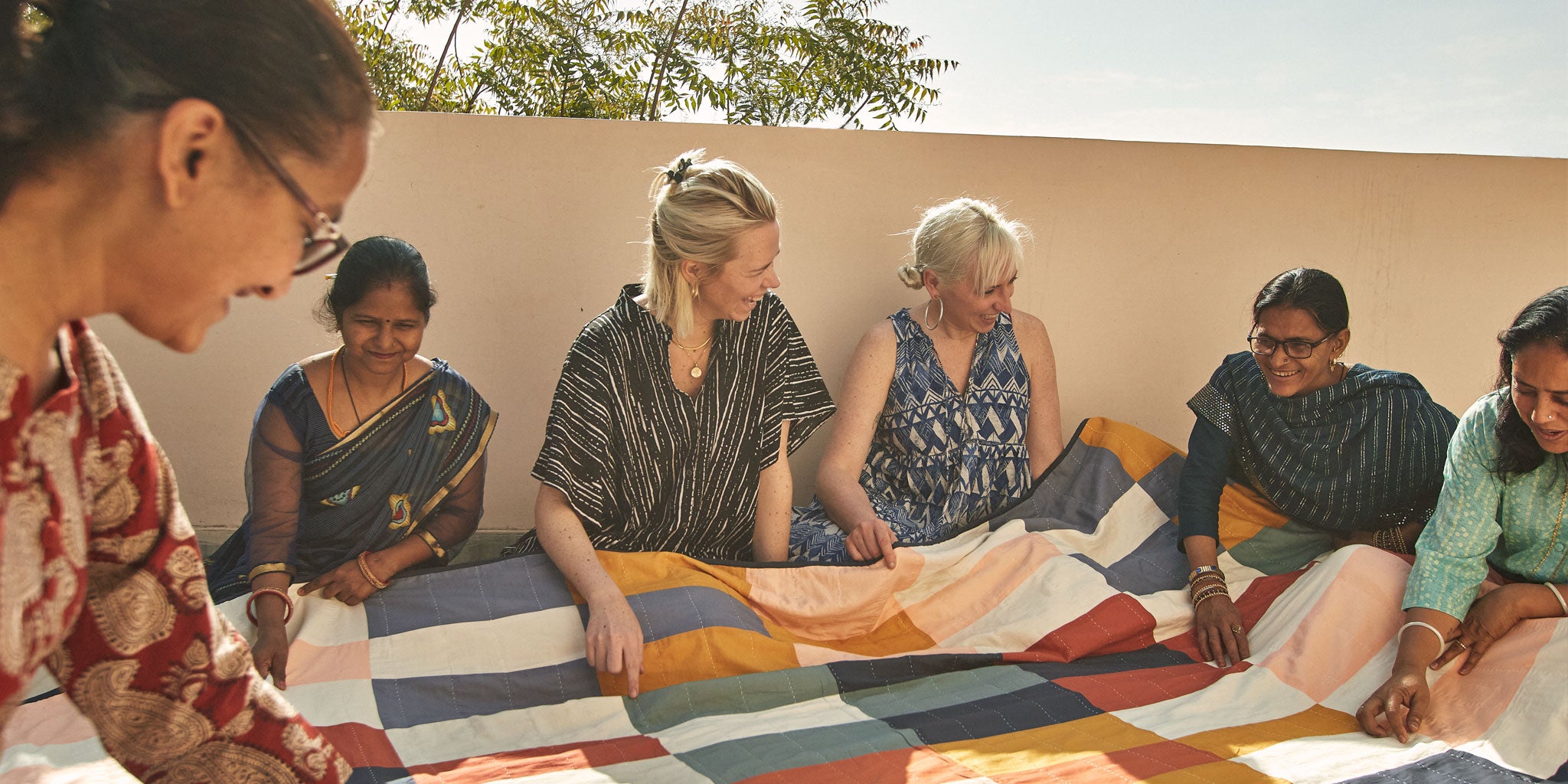 sisters Colleen & Maggie Clines collaborating with artisans in Ajmer, India holding colorful patchwork quilt