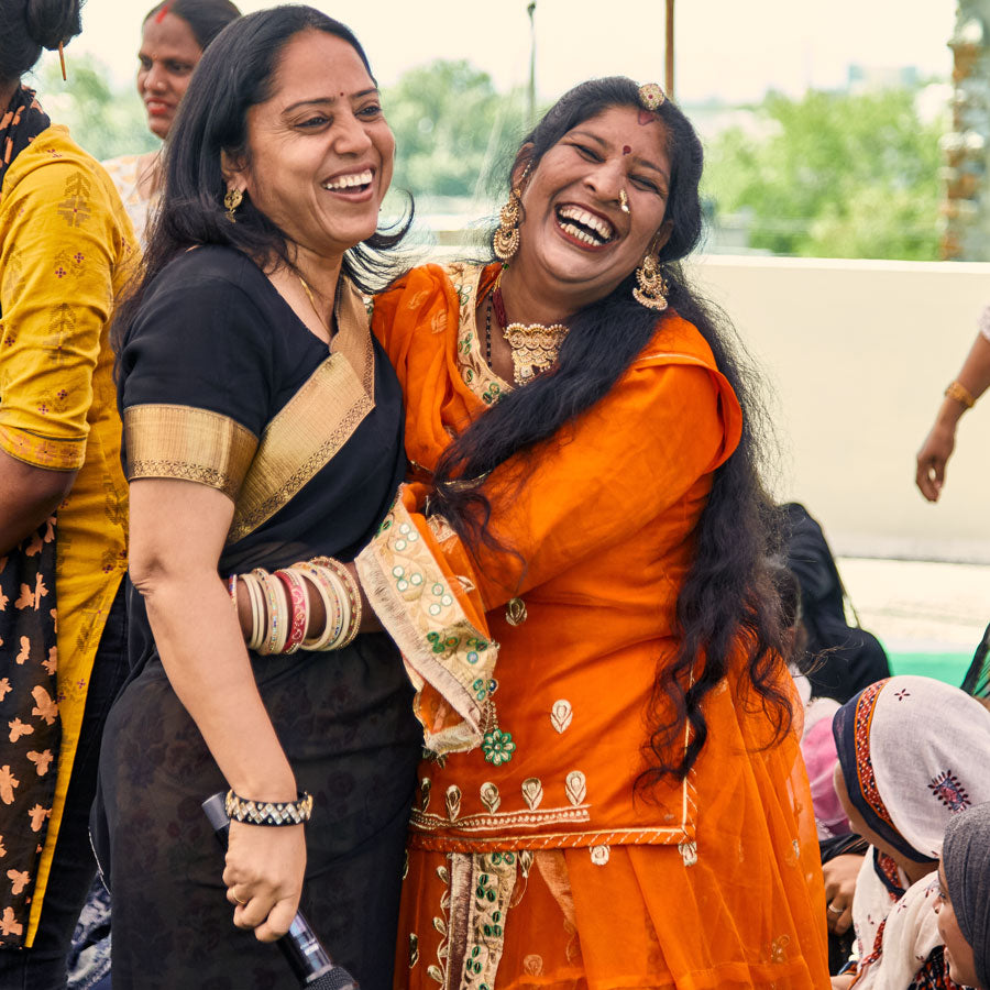 two Indian women hugging and laughing wearing intricate gold accented saris