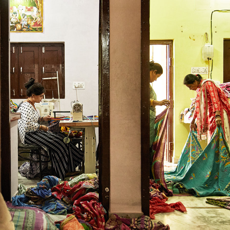 view of 3 artisans in different rooms in Ajmer, India sewing & holding up kantha quilts to ship out