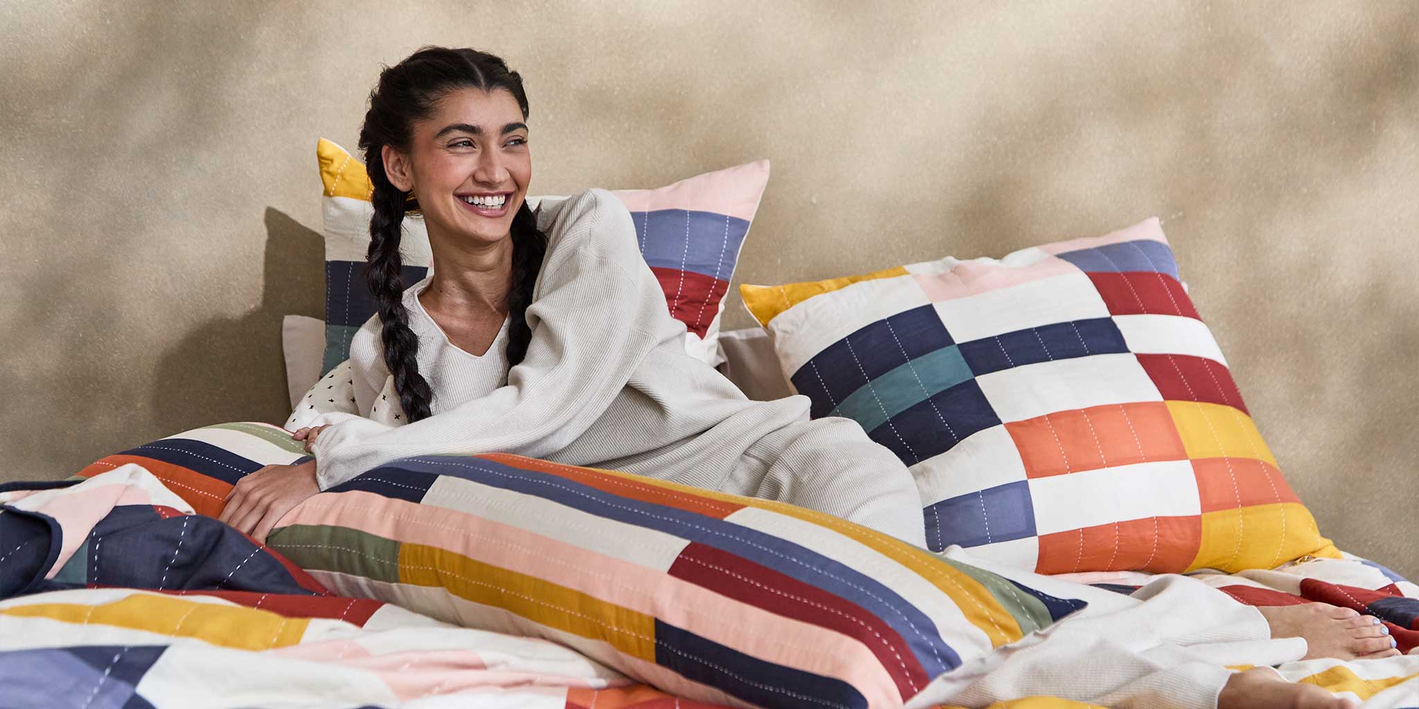 woman laying in bed of colorful rainbow checkered pillows in different shapes and sizes