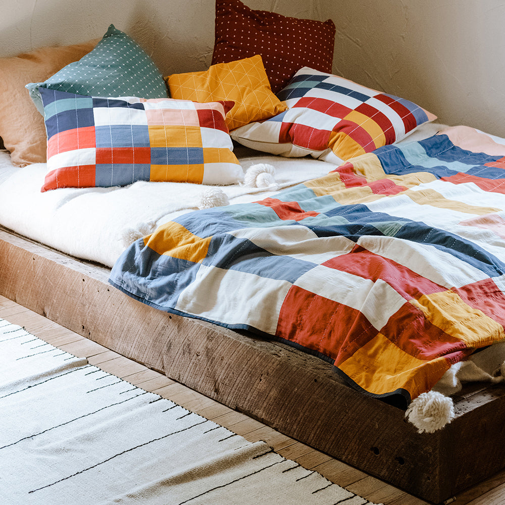 colorful organic cotton quilts & pillows on rustic modern wooden bedframe featuring the multi-check patchwork quilt