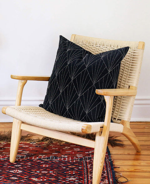 Black geometric-patterned pillow on a wicker chair with a white wall background