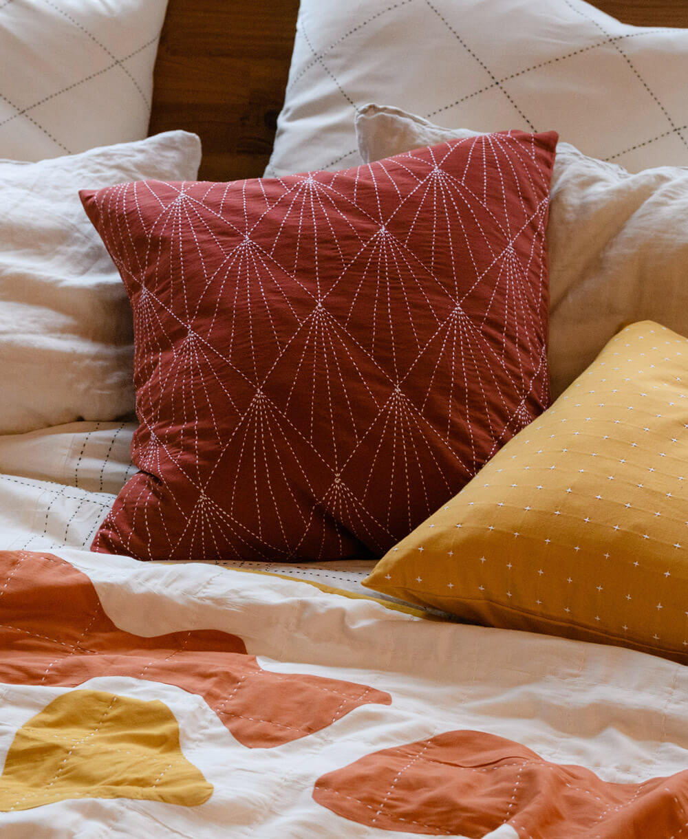 rust red square pillow with hand-stitched embroidery on bed with white and yellow throw pillows