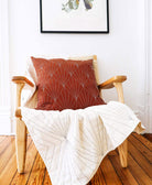 burnt orange square pillow with white embroidery in light wooden chair