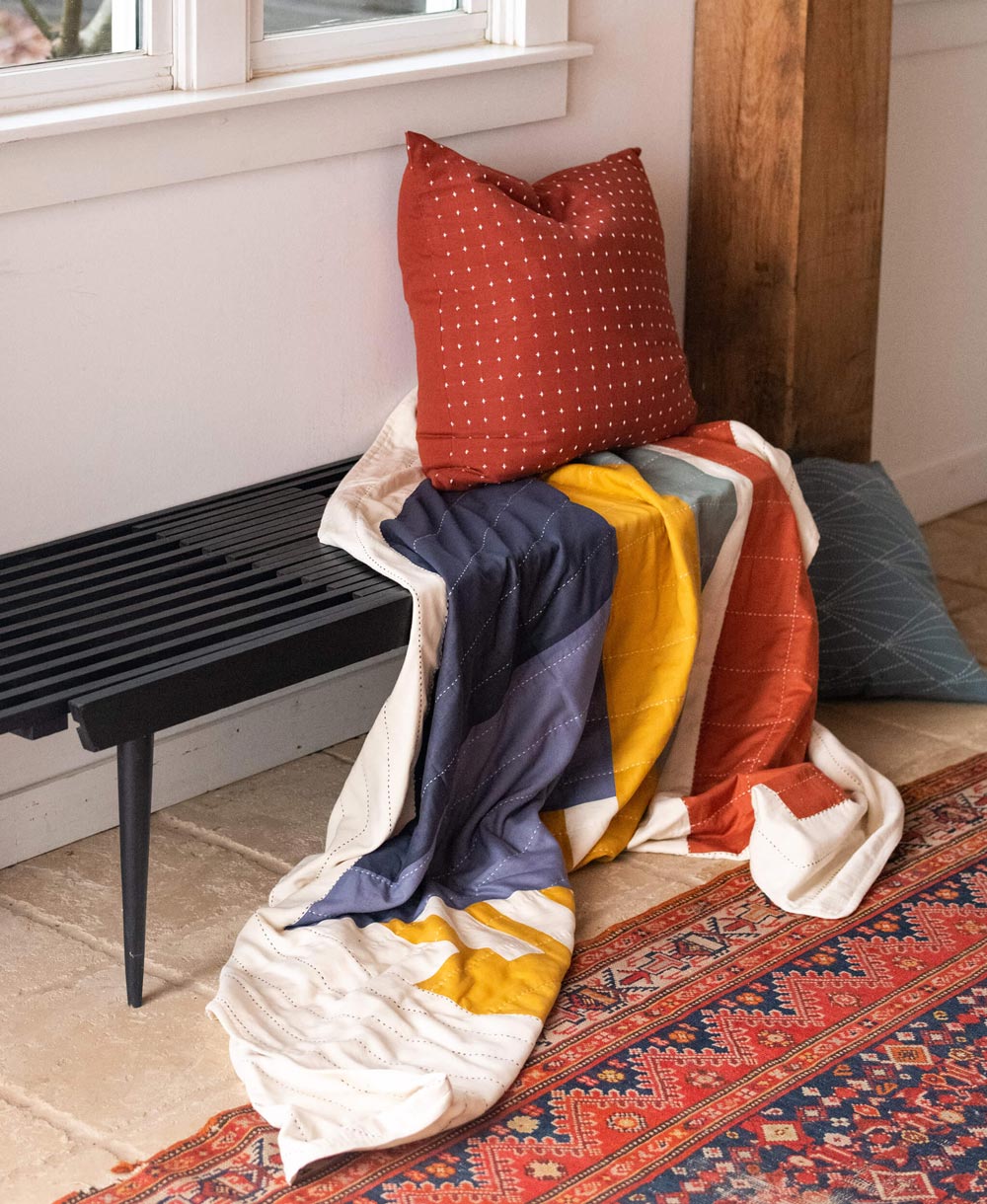 modern patchwork quilt draped over black mid-century modern entryway. bench