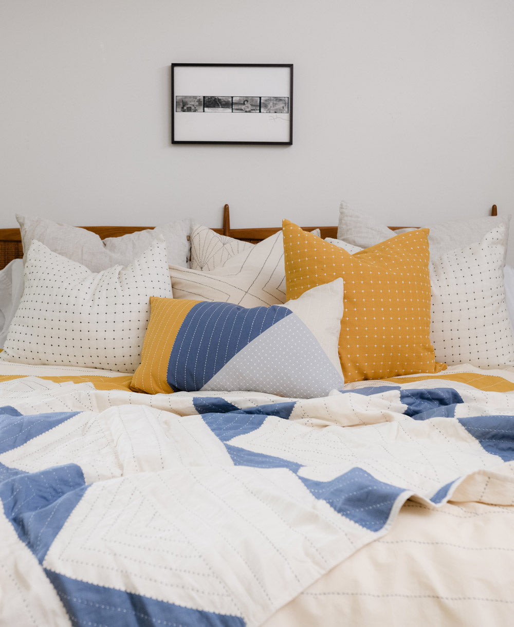 blue and yellow lumbar pillow on all white bed accented with yellow and blue pillows & throws