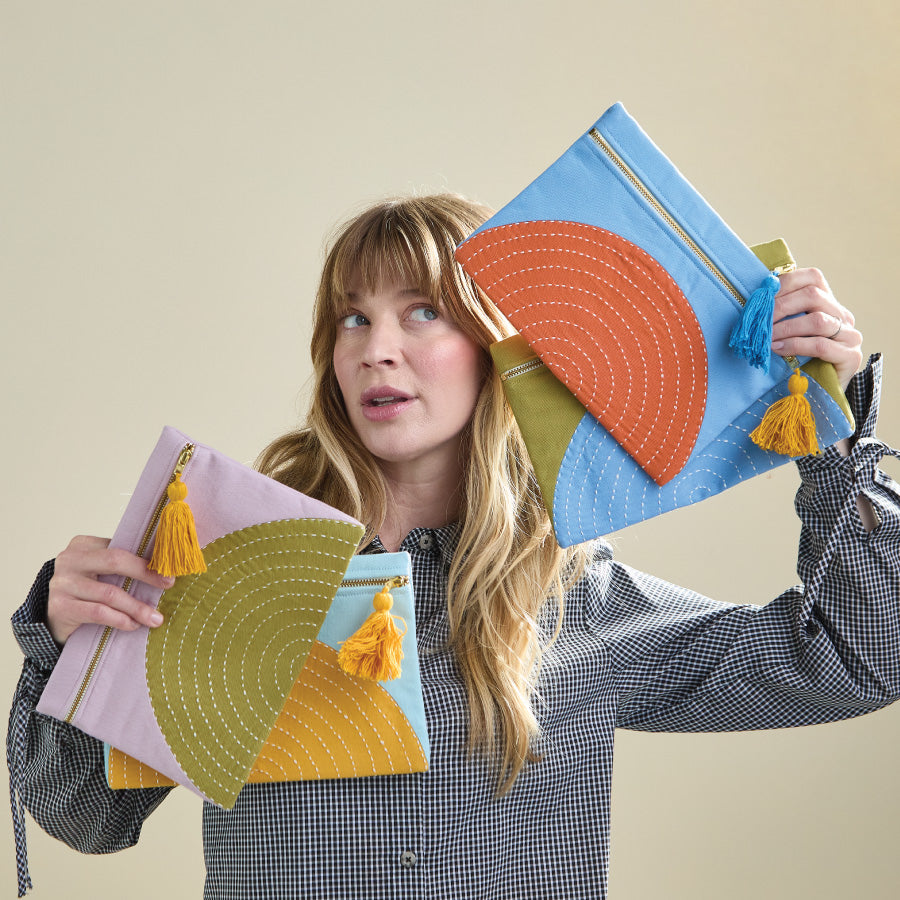 Woman holding colorful geometrically patterned pouches against a plain background
