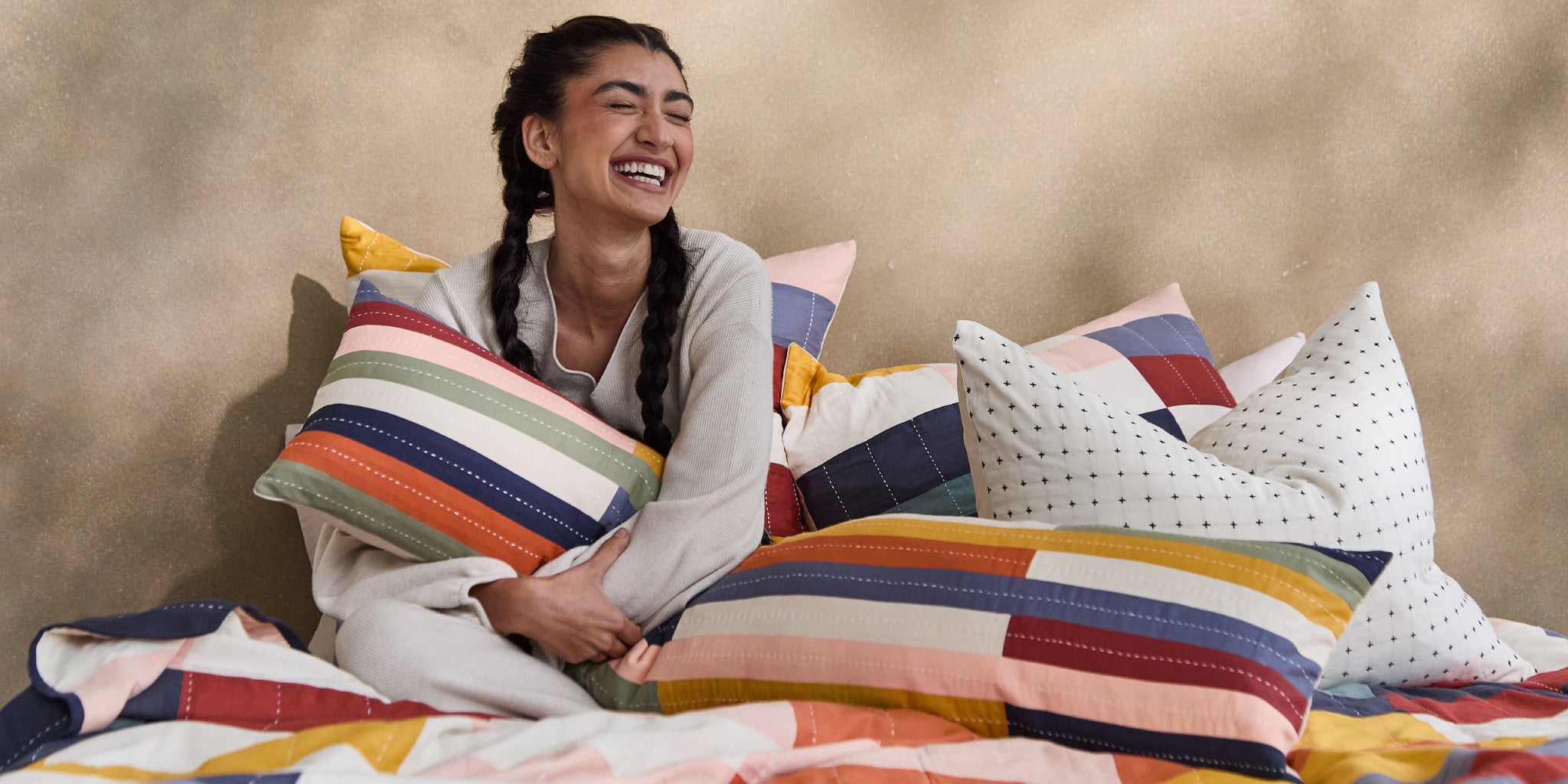 woman in colorful bed of organic cotton rainbow pillows and hand-embroidered modern kantha quilt