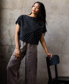 woman wearing a structured boxy black crop top with a geometric white embroidery pattern paired with grey trousers