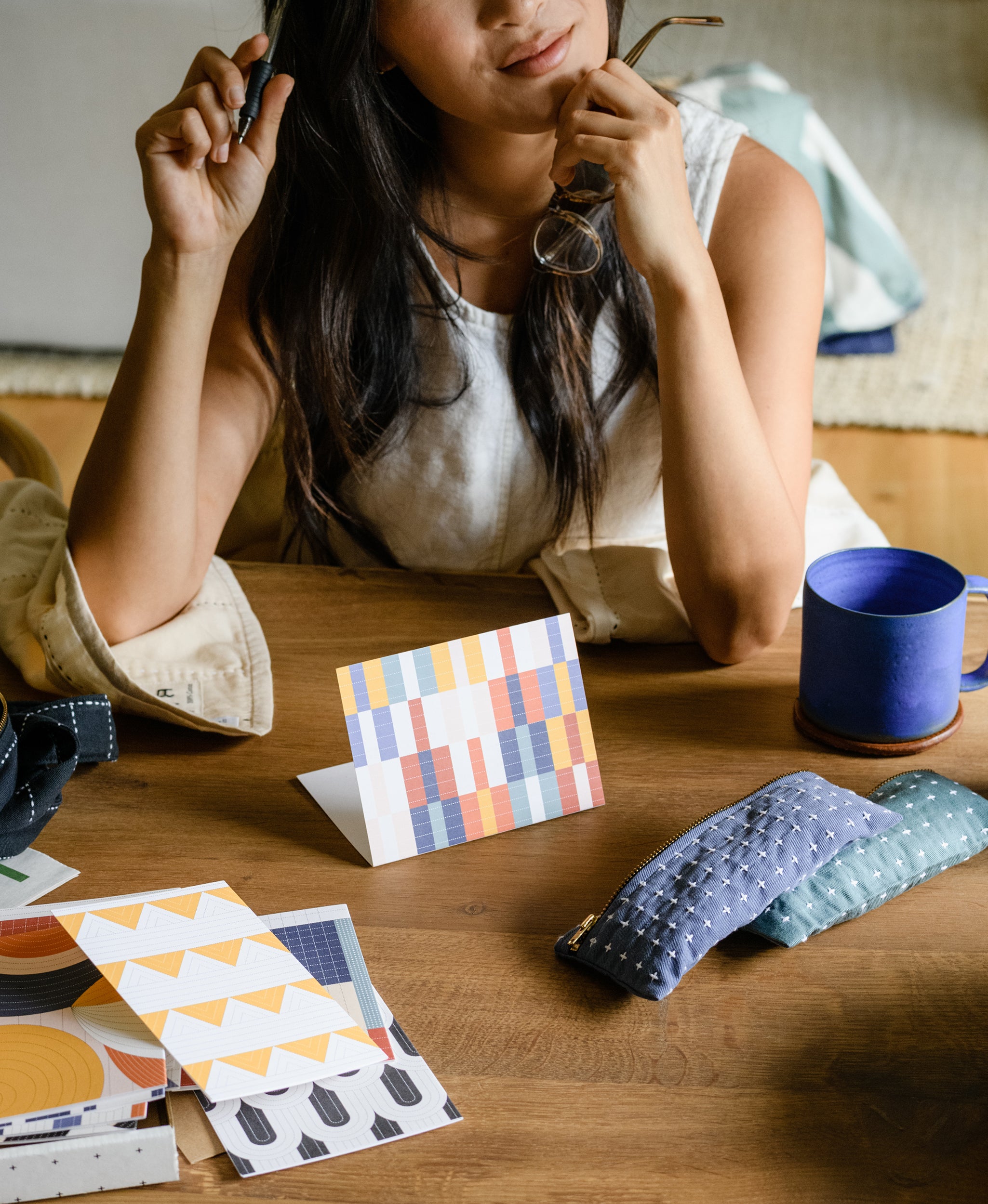 woman writing a thank you note at wooden desk with black gel pen and blue coffee mug