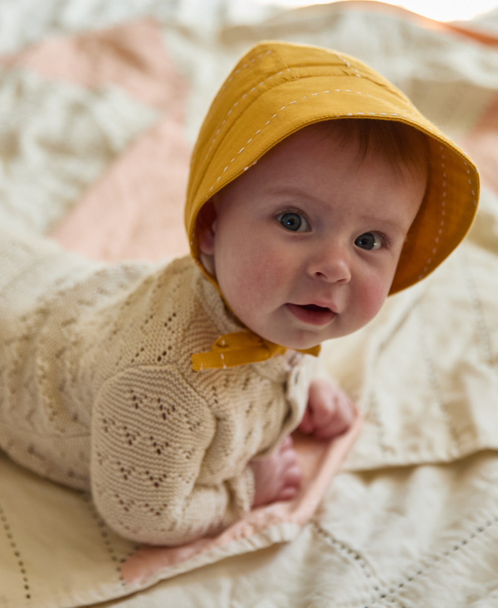 baby girl wearing a yellow brimmed baby bonnet with chin ties made from 100% certified organic cotton