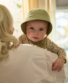 mother carrying baby girl wearing a sage green brimmed baby bonnet with chin ties made from organic cotton