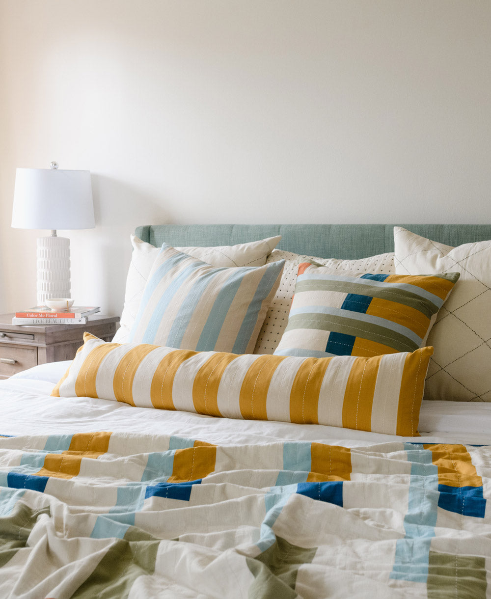 skinny long pillow on bed with mismatched colorful throw pillows on light blue upholstered bed frame