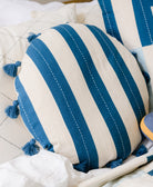 cobalt blue and white striped circle pillow with playful cotton tassels on all white bed