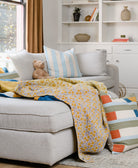 light blue striped square pillow on light grey modular sectional with yellow floral kantha quilt and light brown teddy bear