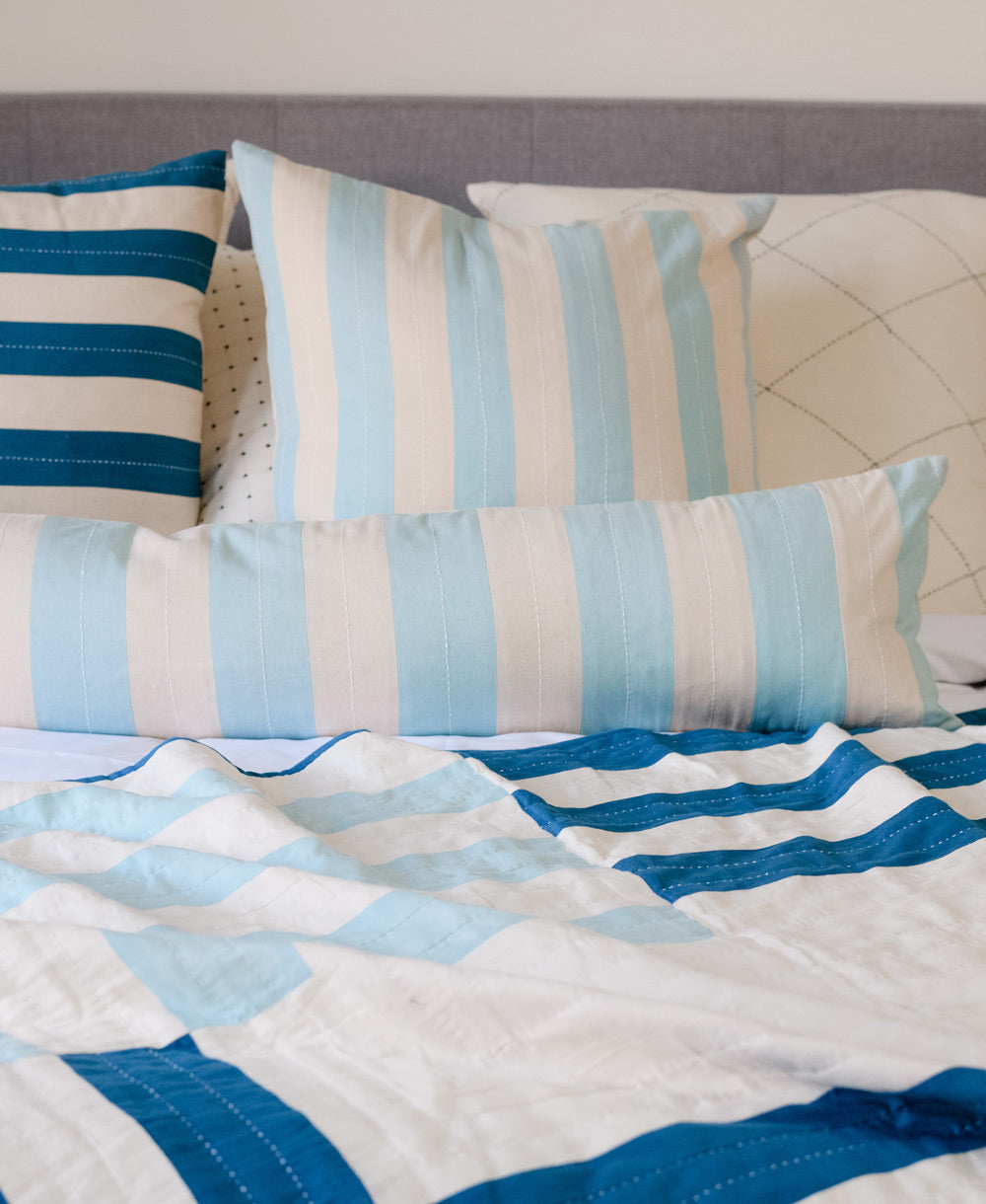 light blue vertically stripe throw pillow with cobalt blue striped pillows on all white bed