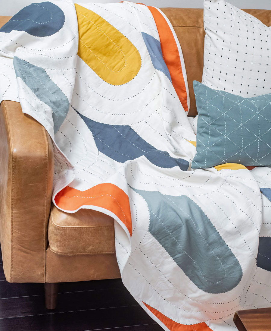 modern kantha quilt in bright rainbow colors draped over the arm of brown leather sofa