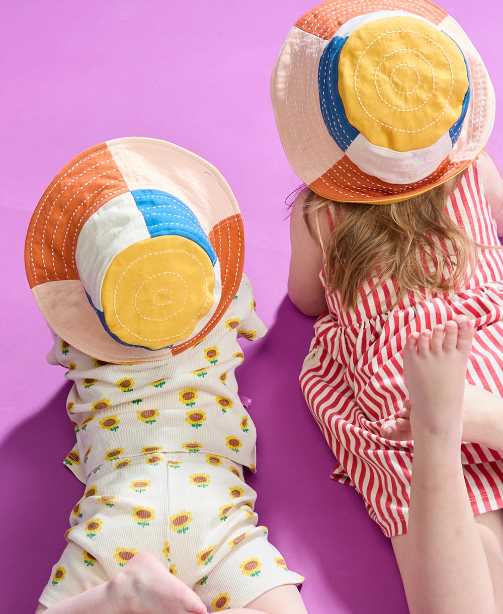 two little girls wearing checkered bucket hats laying on the ground