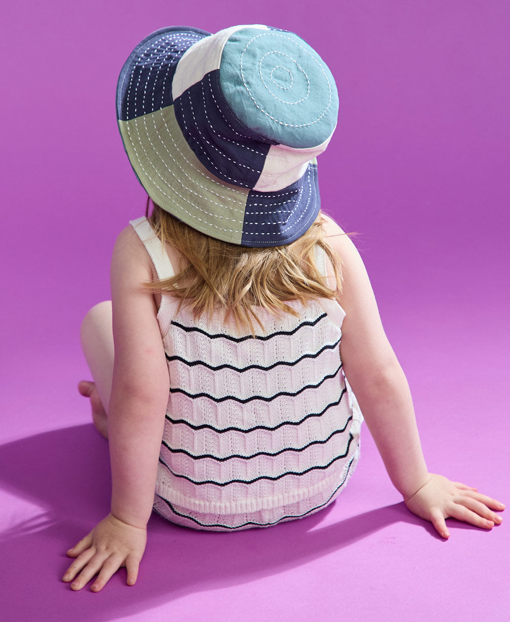 little girl sitting on pink backdrop wearing checkered bucket hat in sage