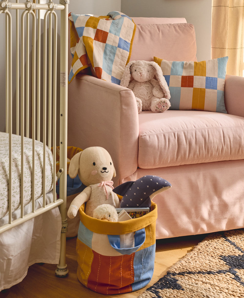 Children's room with a crib, pink sofa, and colorful toys in storage bin basket made from organic cotton