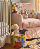 Children's room with a crib, pink sofa, and colorful toys in storage bin basket made from organic cotton