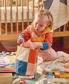 toddler girl putting wooden blocks into round cloth storage bin in bold checkered rainbow design