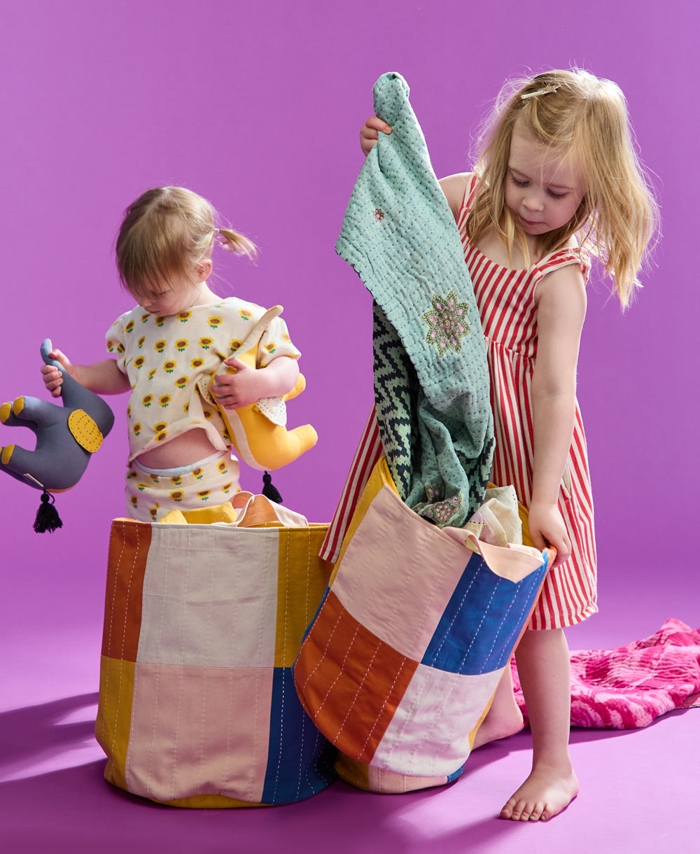 two little girls pulling quilts and toys out of checkered fabric storage bin