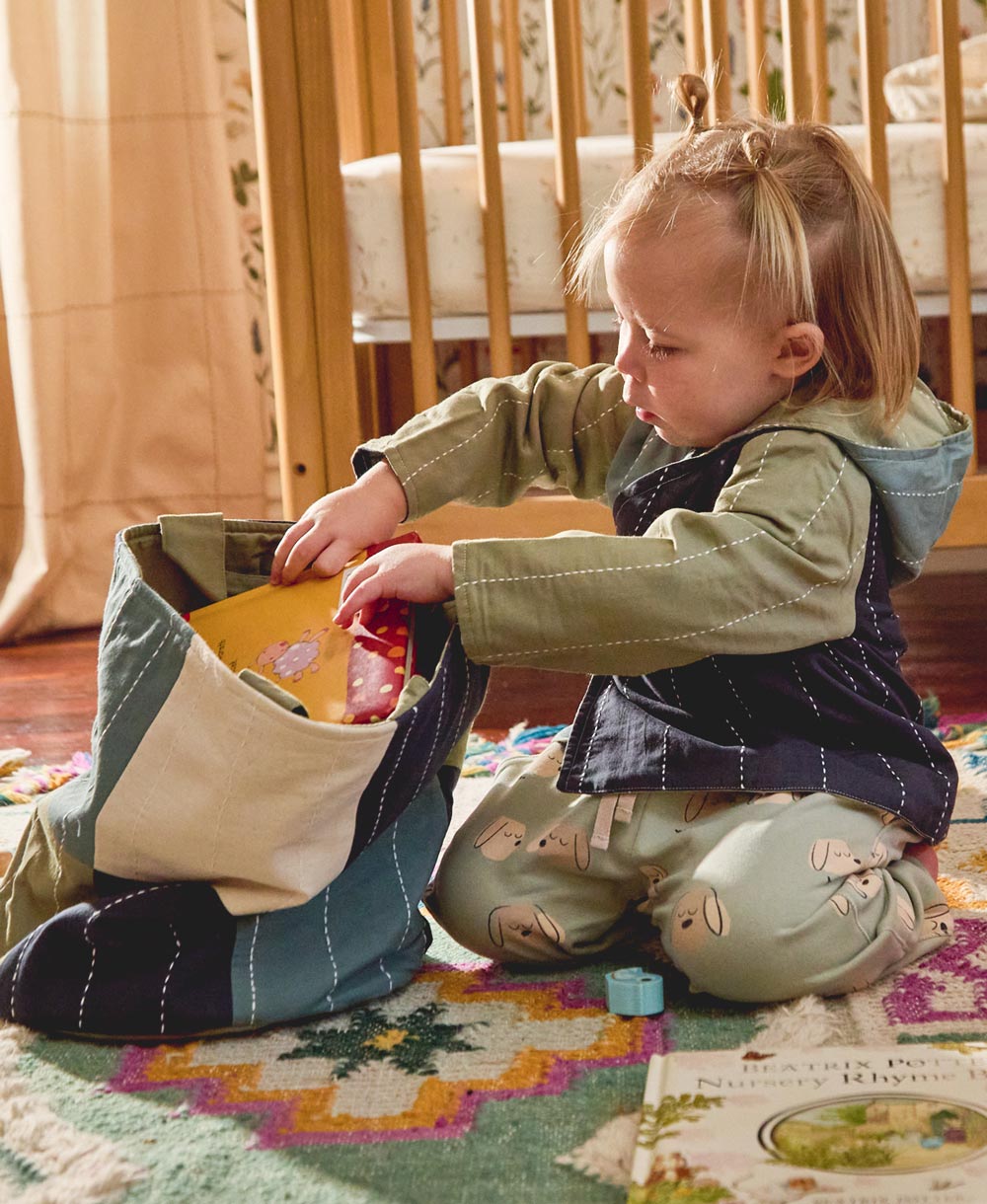 toddler putting toys away in bedroom into round fabric basket in blue and green made from organic cotton