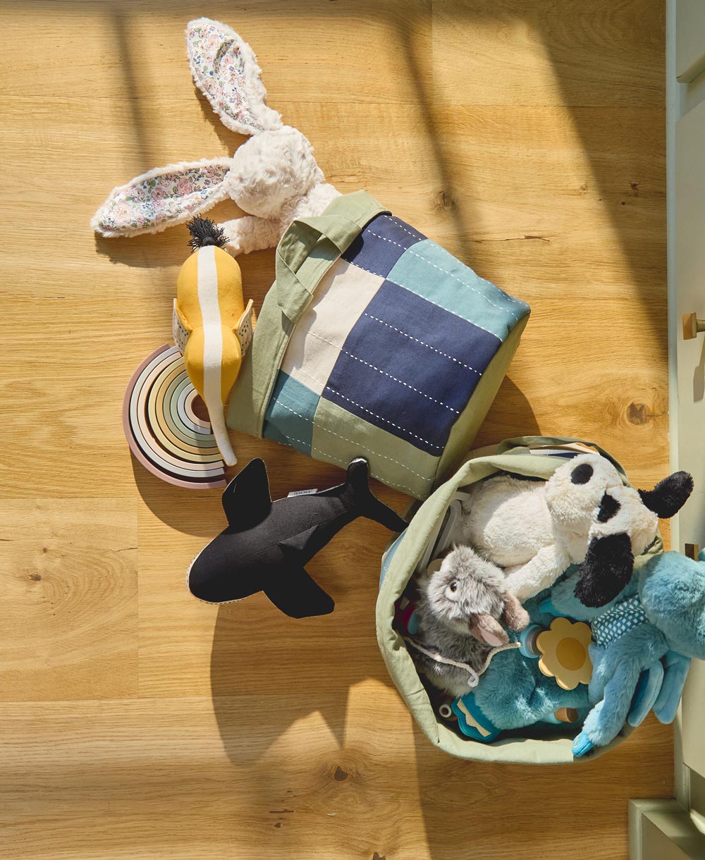  children's toys, including a plush bunny, rings, and animal figures on a wooden surface in a fabric basket in shades of blue and green