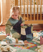 toddler putting wooden blocks in bedroom into blue and green small fabric basket