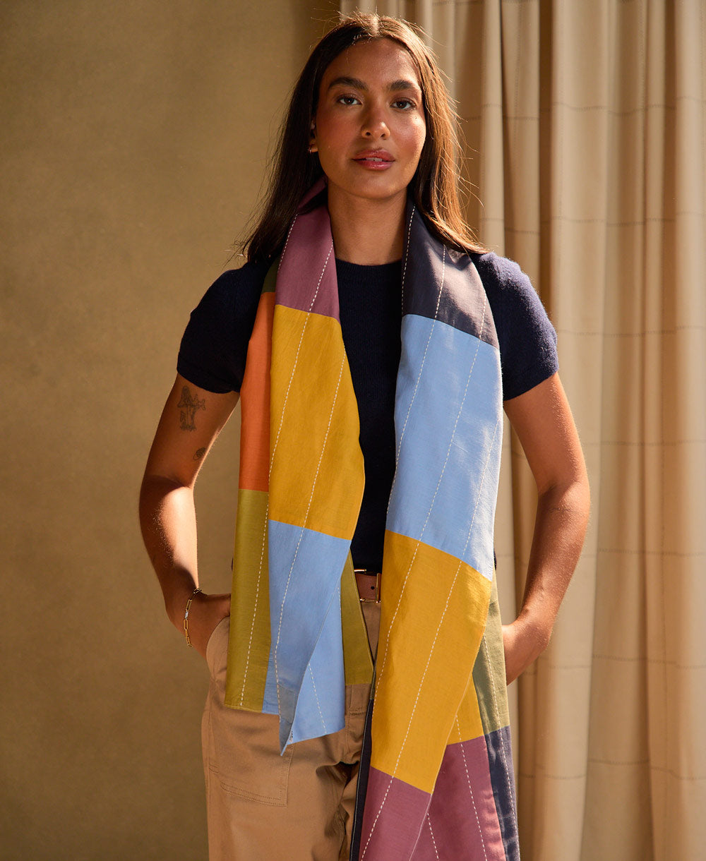 Woman wearing a colorful checkered patchwork long scarf against a beige curtain background