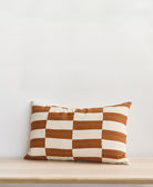 camel and white checkered lumbar pillow with removable down feather insert sitting on light wooden bench