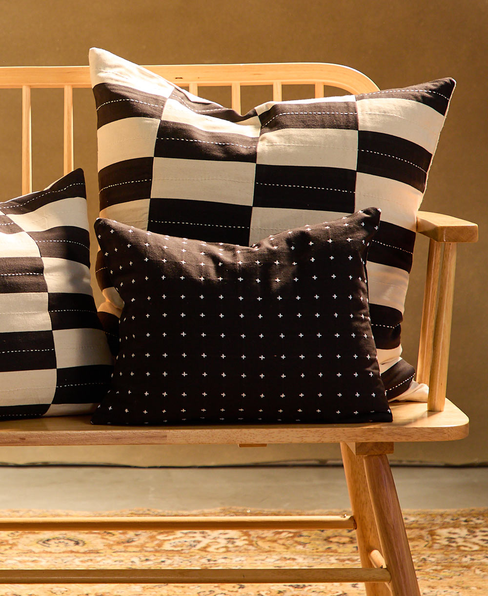 Black and white checkered and patterned pillows on a wooden chair against a beige wall.