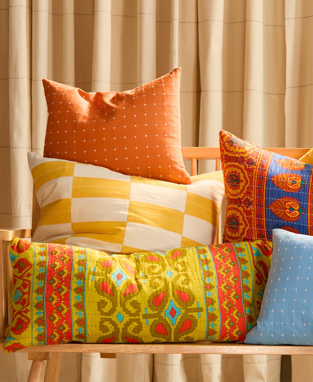 Colorful patterned and checkered cushions on a wooden chair with a beige curtain background