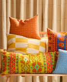 Colorful patterned and checkered cushions on a wooden chair with a beige curtain background
