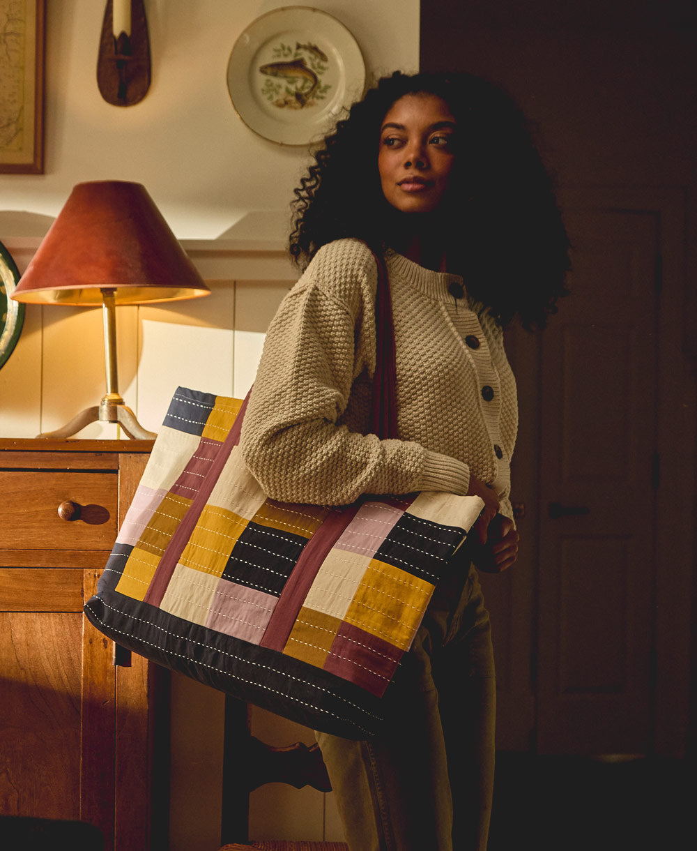 woman carrying a checkered canvas tote bag on her shoulder in tones of lilac, navy and yellow