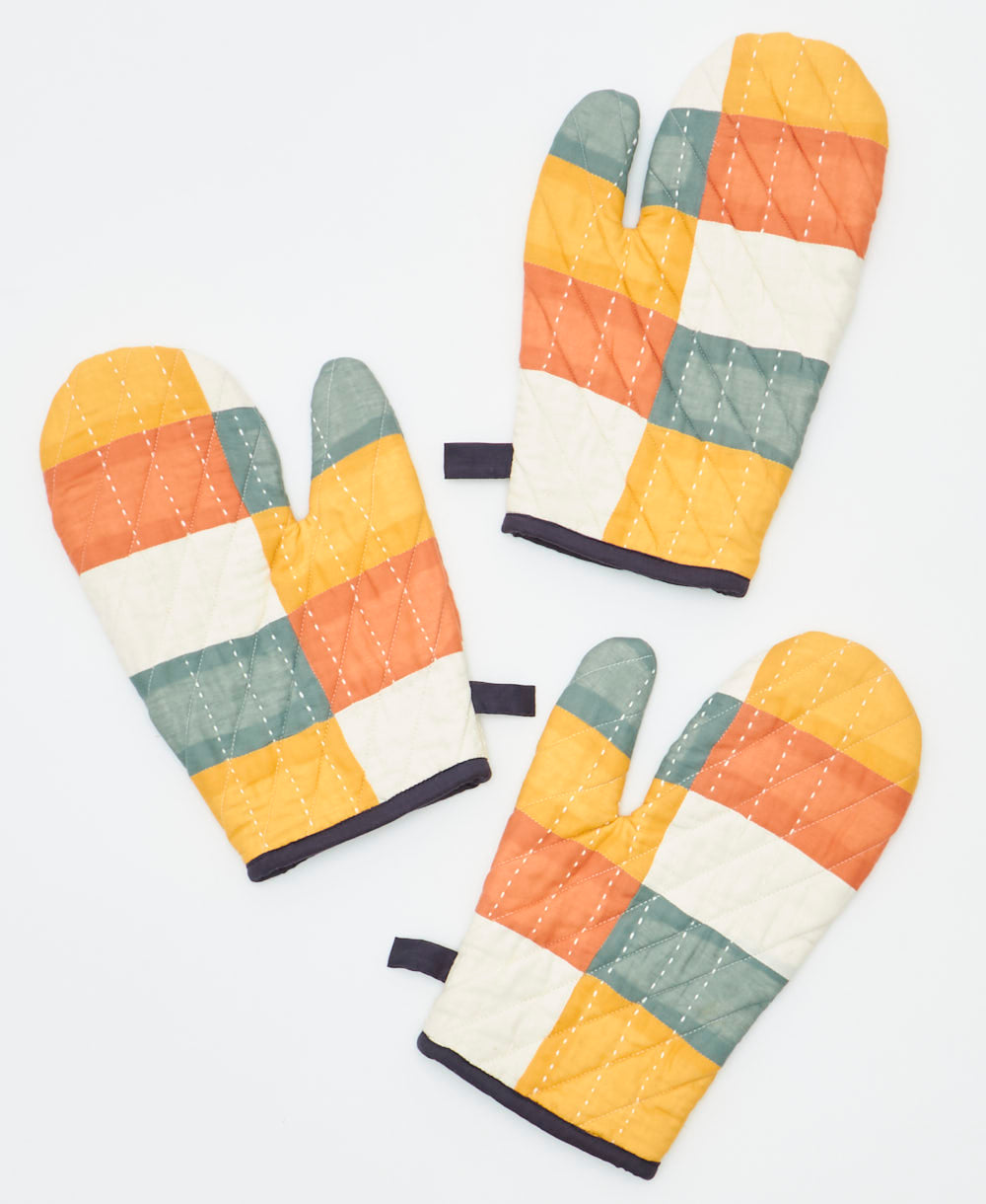 Three patchwork oven mitts in different color patterns on a white background